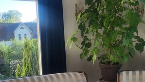 A living room with a sofa, a coffee table, a potted plant, and a view through a window. - Vacation apartment for 5 people at Gut Hange by the forest and lake (Freren)
