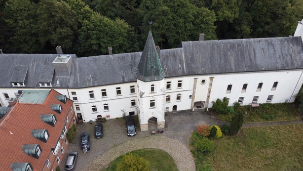 An aerial view of a large building with a central tower, multiple windows, and a courtyard with parked cars. - Vacation apartment for 5 people at Gut Hange by the forest and lake (Freren)