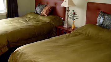 A hotel room with two beds, a nightstand with a lamp, and a window with curtains.