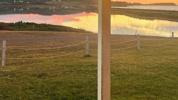 A serene lakeside view with a wooden deck and a covered area, reflecting the sunset. - Island Sunset Resort (Belle Côte)
