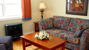A living room with a patterned sofa, a wooden coffee table with flowers, a fireplace, and a lamp. - Island Sunset Resort (Belle Côte)