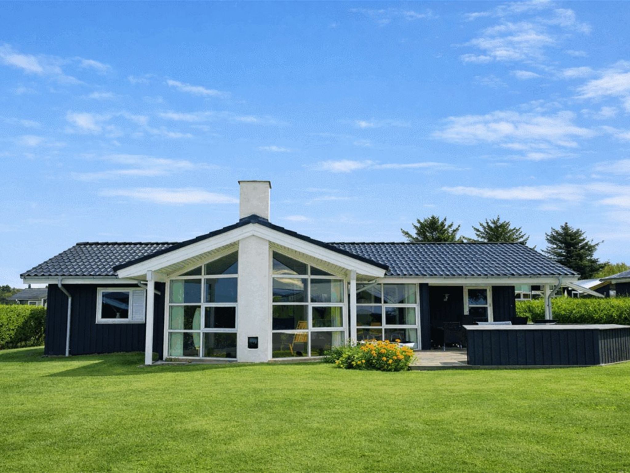 Een modern huis met een grote glazen gevel, een donker dak en een verzorgd gazon.