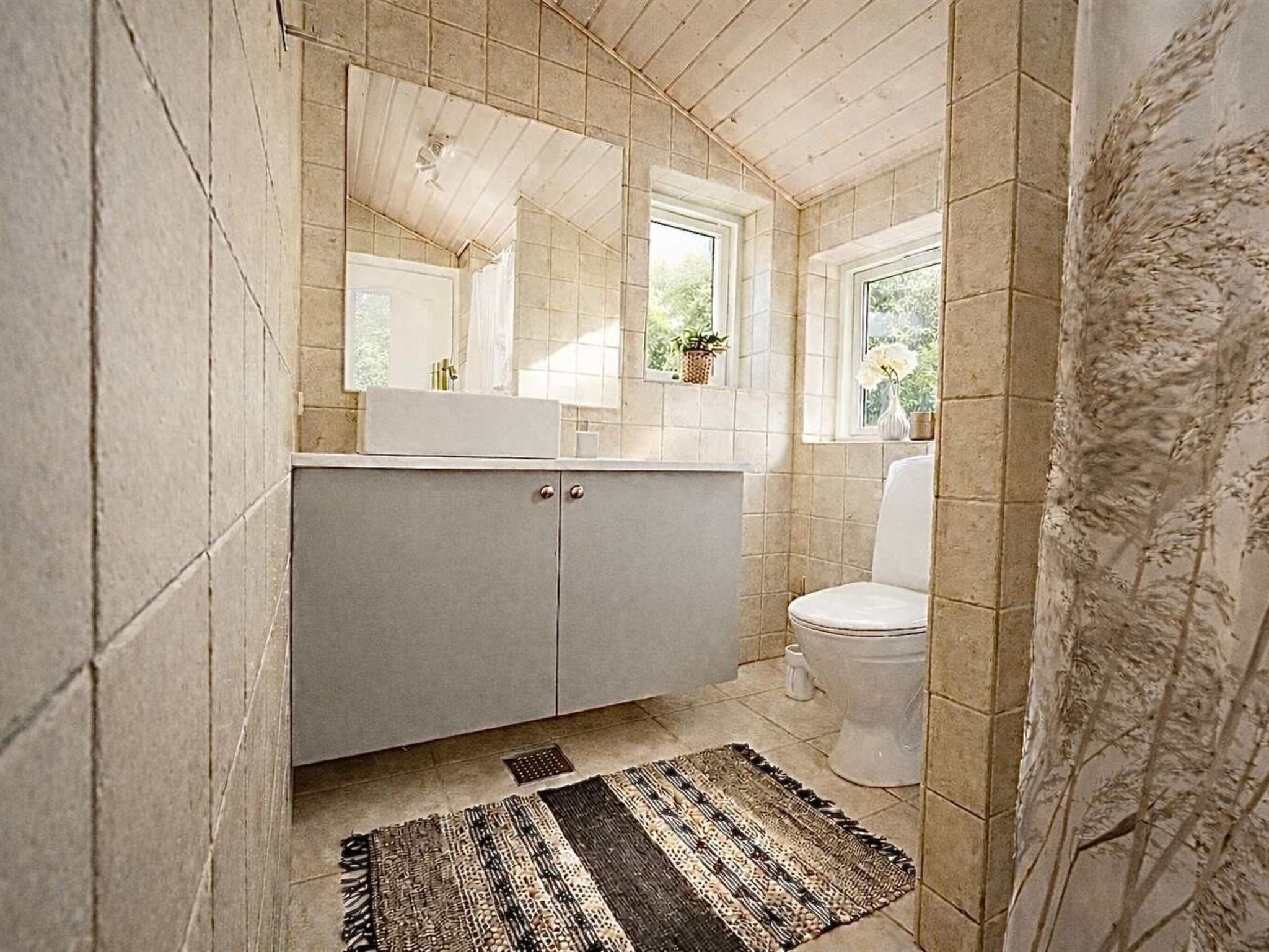 A bathroom with a tiled floor, a sink, a toilet, and a window.