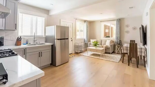 Una cocina moderna con una isla central, un comedor con mesa y sillas, y una sala de estar con sofá y televisor.