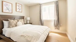 Un dormitorio con una cama, una mesita de noche, una lámpara y dos cuadros en la pared.