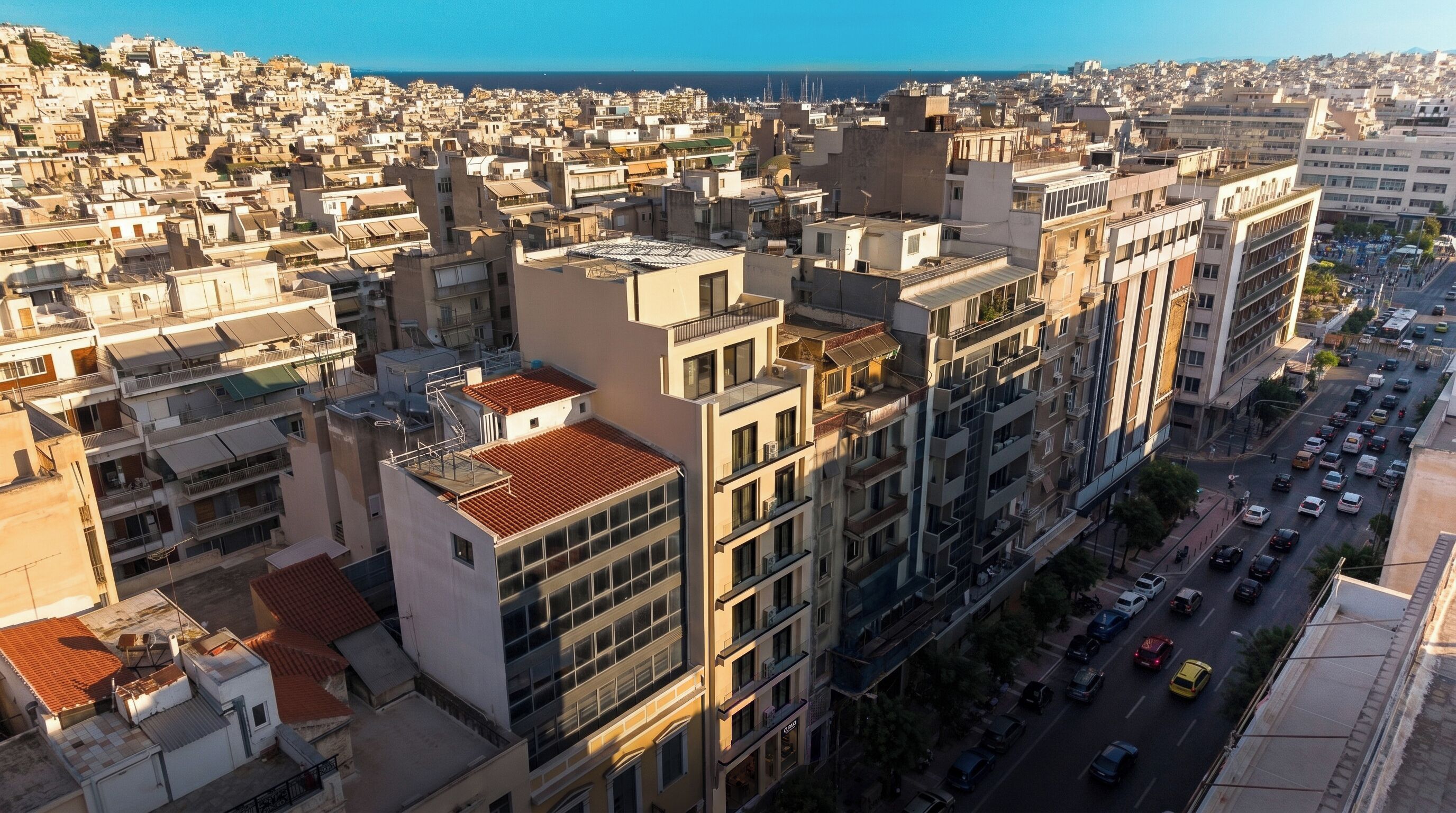 A high-rise building with multiple balconies, a busy street below, and a view of the sea in the background.