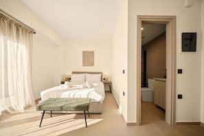 A modern bedroom with a bed, bedside tables, a bench, a painting, and a view of a hallway leading to a bathroom.