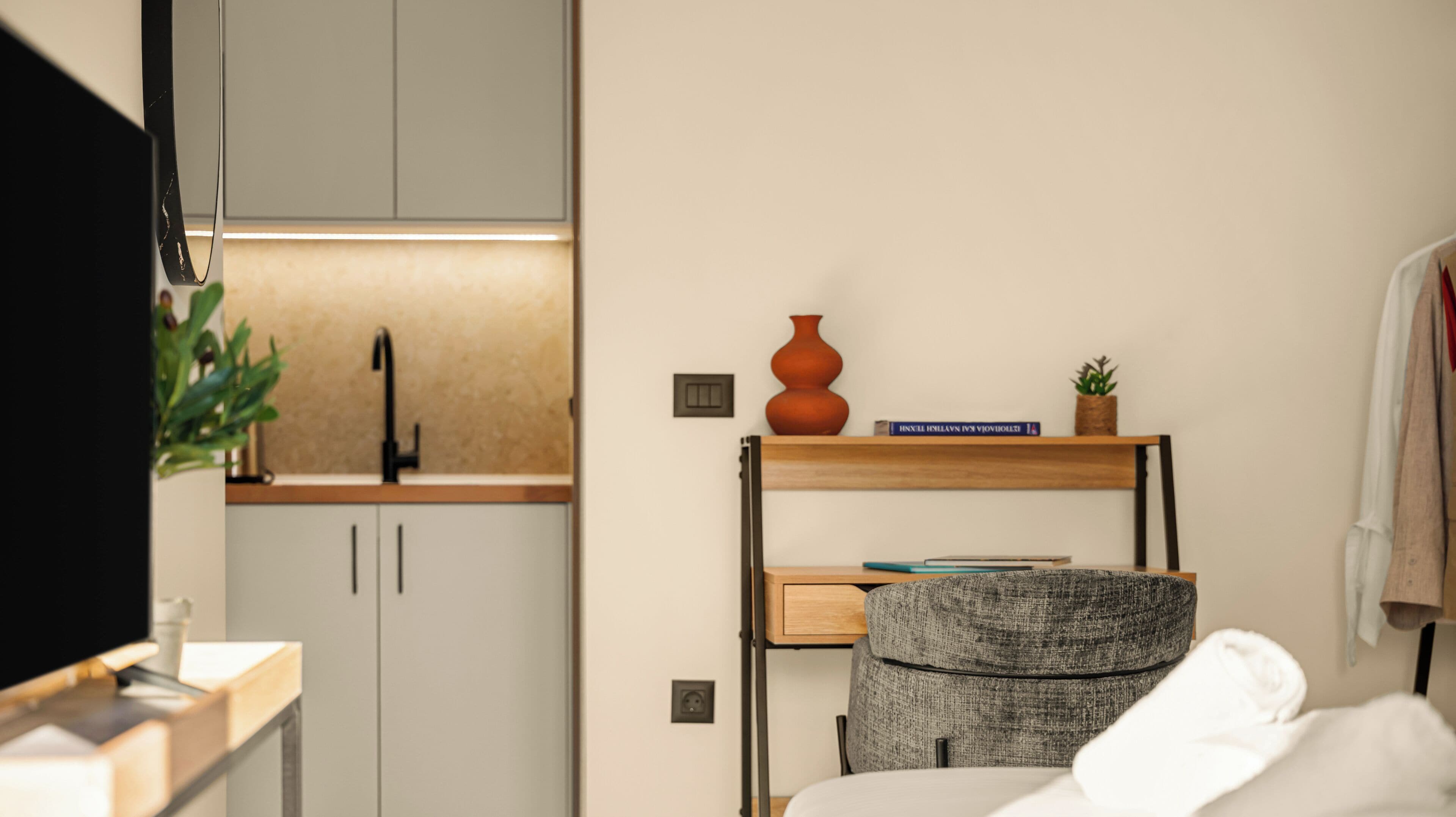 Ein kompaktes Hotelzimmer mit Küchenzeile, einem Bett, einem kleinen Schreibtisch und einem Stuhl.