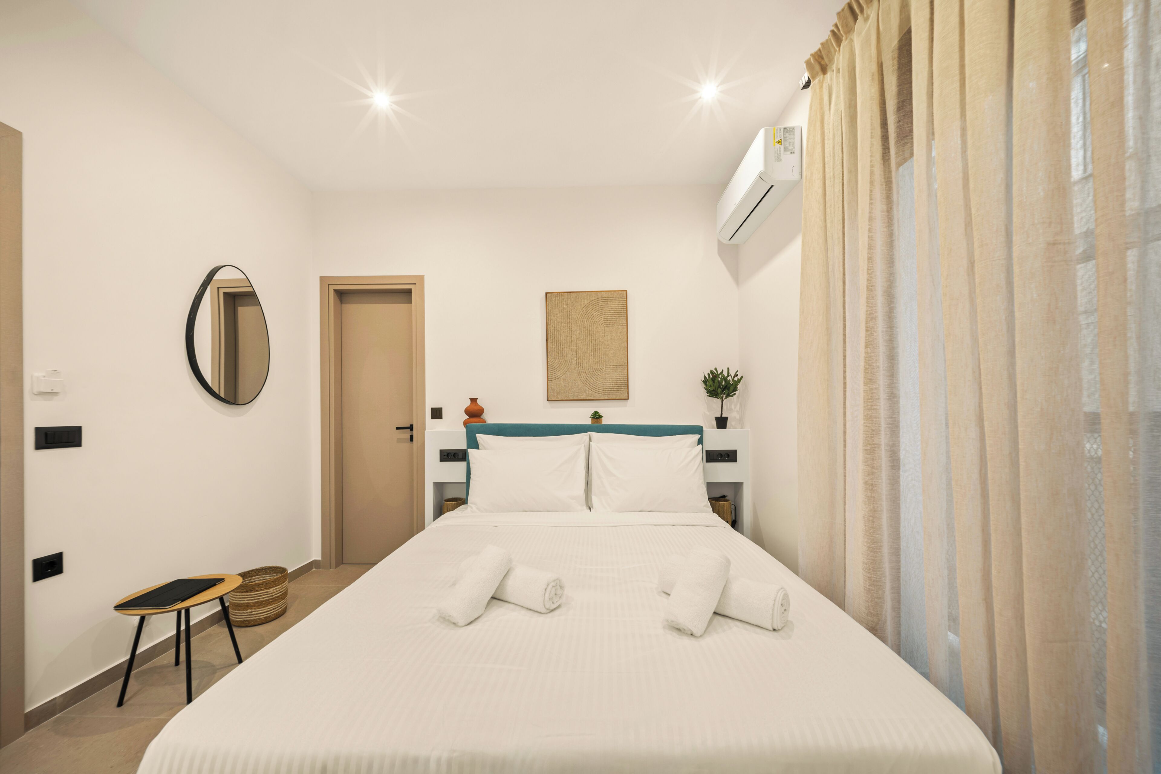 Une chambre d’hôtel comprenant un lit, une table de chevet, une chaise, un miroir fixé au mur, une porte et un appareil de climatisation.