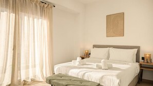 A hotel room with a bed, a bedside table with a lamp, a bench, and sheer curtains. - Ormos Piraeus (Piraeus)