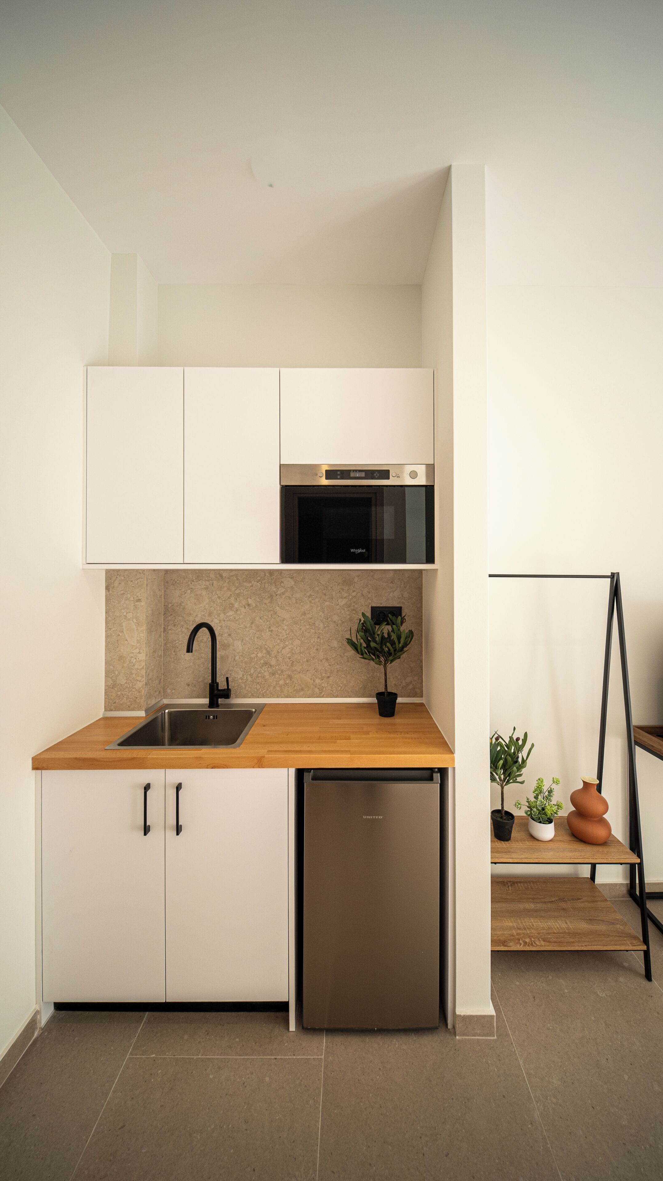 A compact kitchen with white cabinets, a stainless steel sink, a built-in oven, and a compact dishwasher.