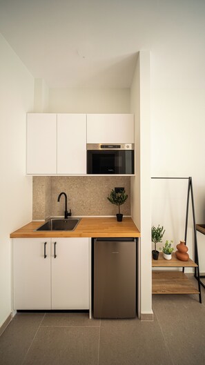 A compact kitchen with white cabinets, a stainless steel sink, a built-in oven, and a compact dishwasher. - Ormos Piraeus (Piraeus)