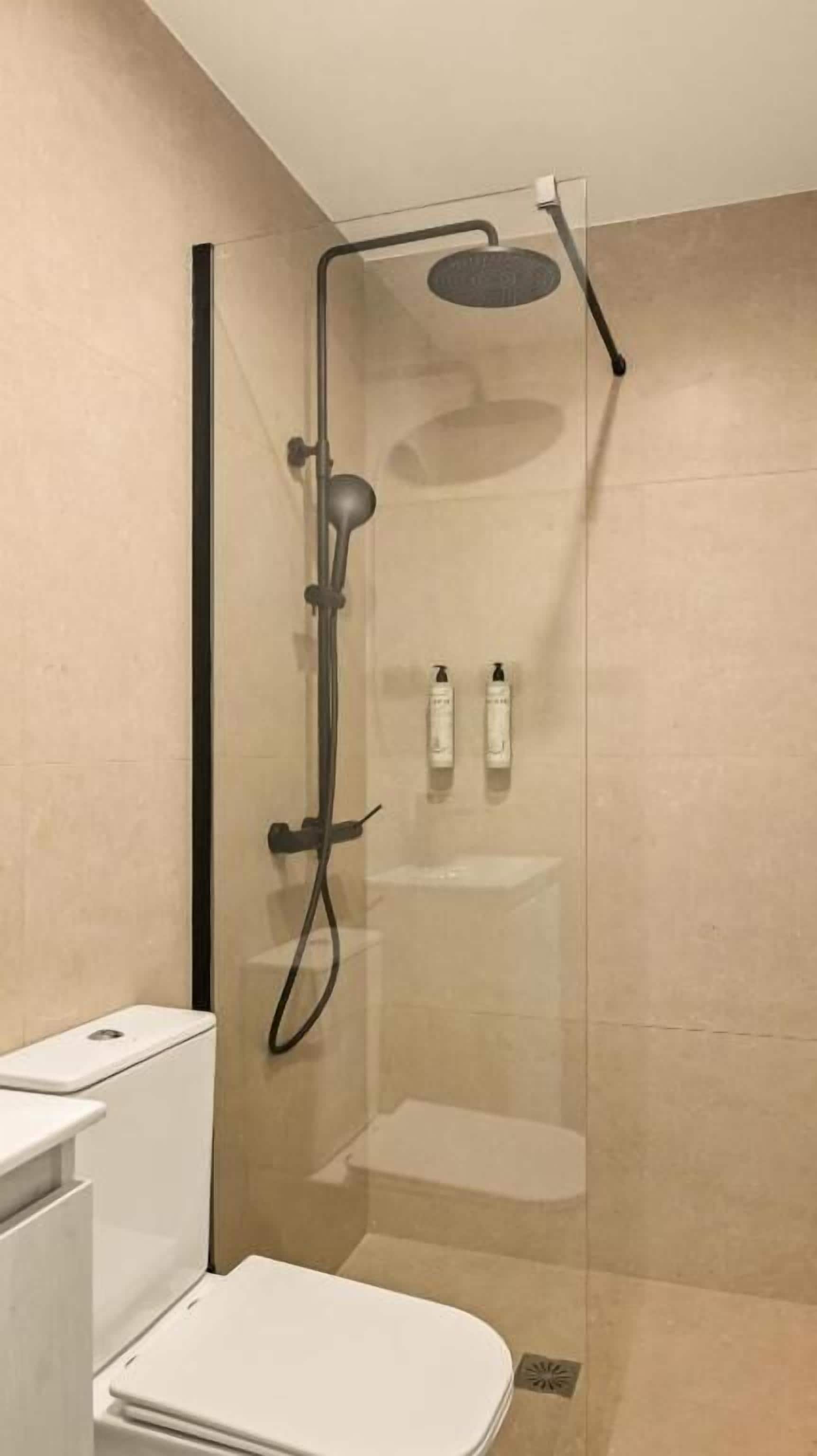 Une salle de bain moderne avec une douche à parois de verre, des toilettes blanches et un petit lavabo blanc.