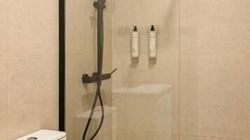Une salle de bain moderne avec une douche à parois de verre, des toilettes blanches et un petit lavabo blanc.