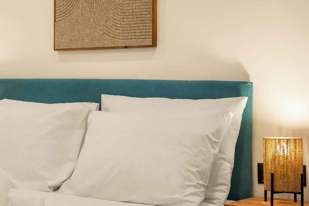 Un lit avec une literie blanche, une tête de lit de couleur turquoise et une œuvre d’art accrochée au mur.