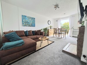 Un salón con un sofá marrón, una mesa de centro, un cuadro y una zona de comedor con sillas y una mesa.