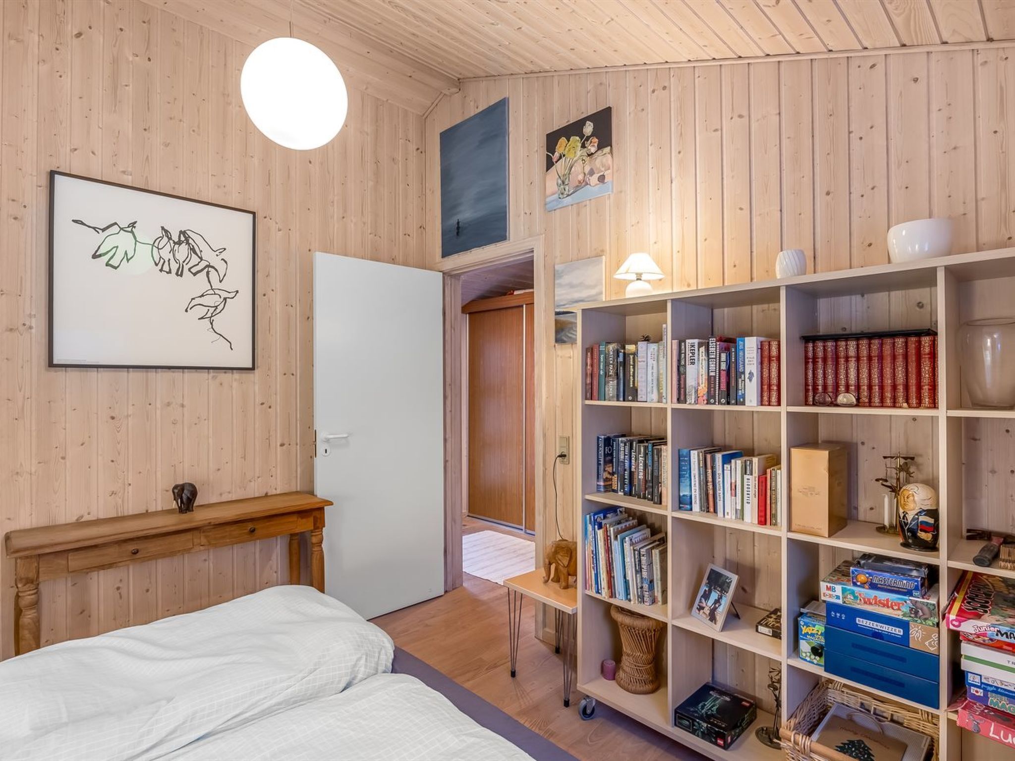 A bedroom with a bed, a wooden headboard, a bookshelf, and a door leading to another room.