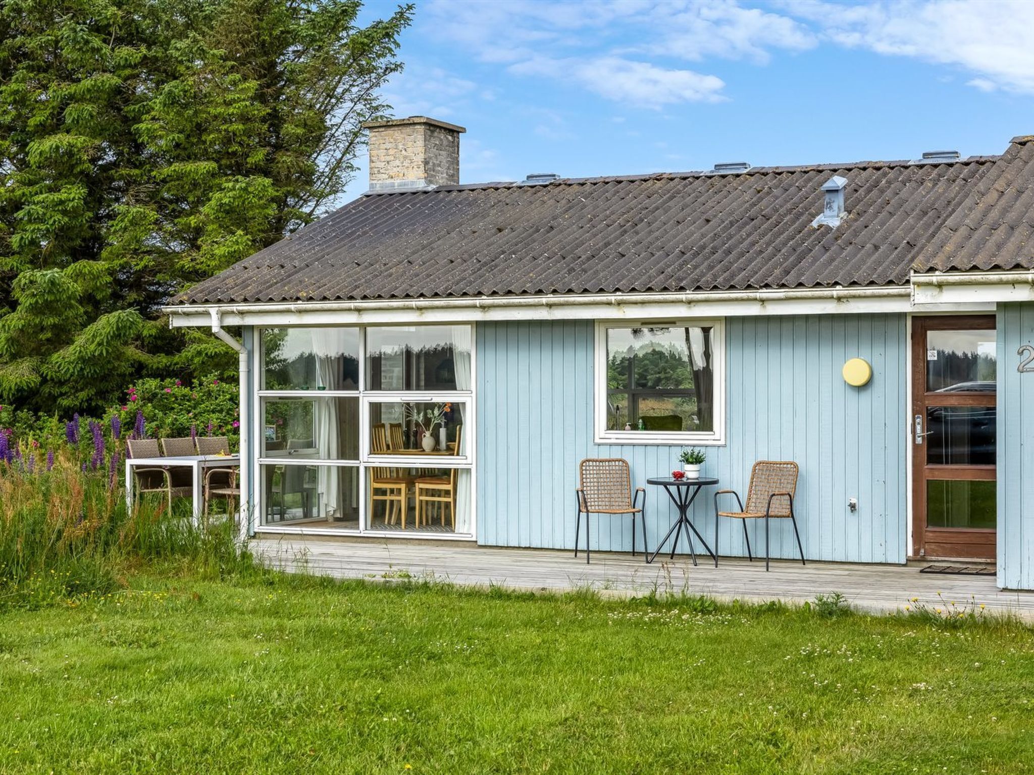 Una casa con un amplio ventanal, una terraza de madera y una puerta.