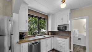Een moderne keuken met witte kasten, roestvrijstalen apparatuur, een groot raam en een magnetron.
