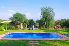 A rectangular swimming pool with a tiled deck, surrounded by a grassy lawn and trees.