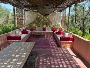 An outdoor seating area with a woven ceiling, cushioned benches, and a patterned rug.