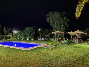 A swimming pool surrounded by grass, trees, and outdoor furniture.