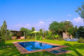 A swimming pool with a surrounding grassy area, a pergola, and a small pavilion.