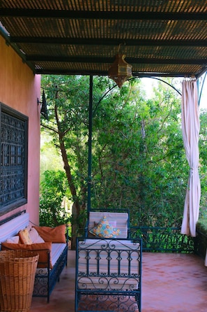 A covered patio with a bed, a wicker basket, and a hanging lantern.