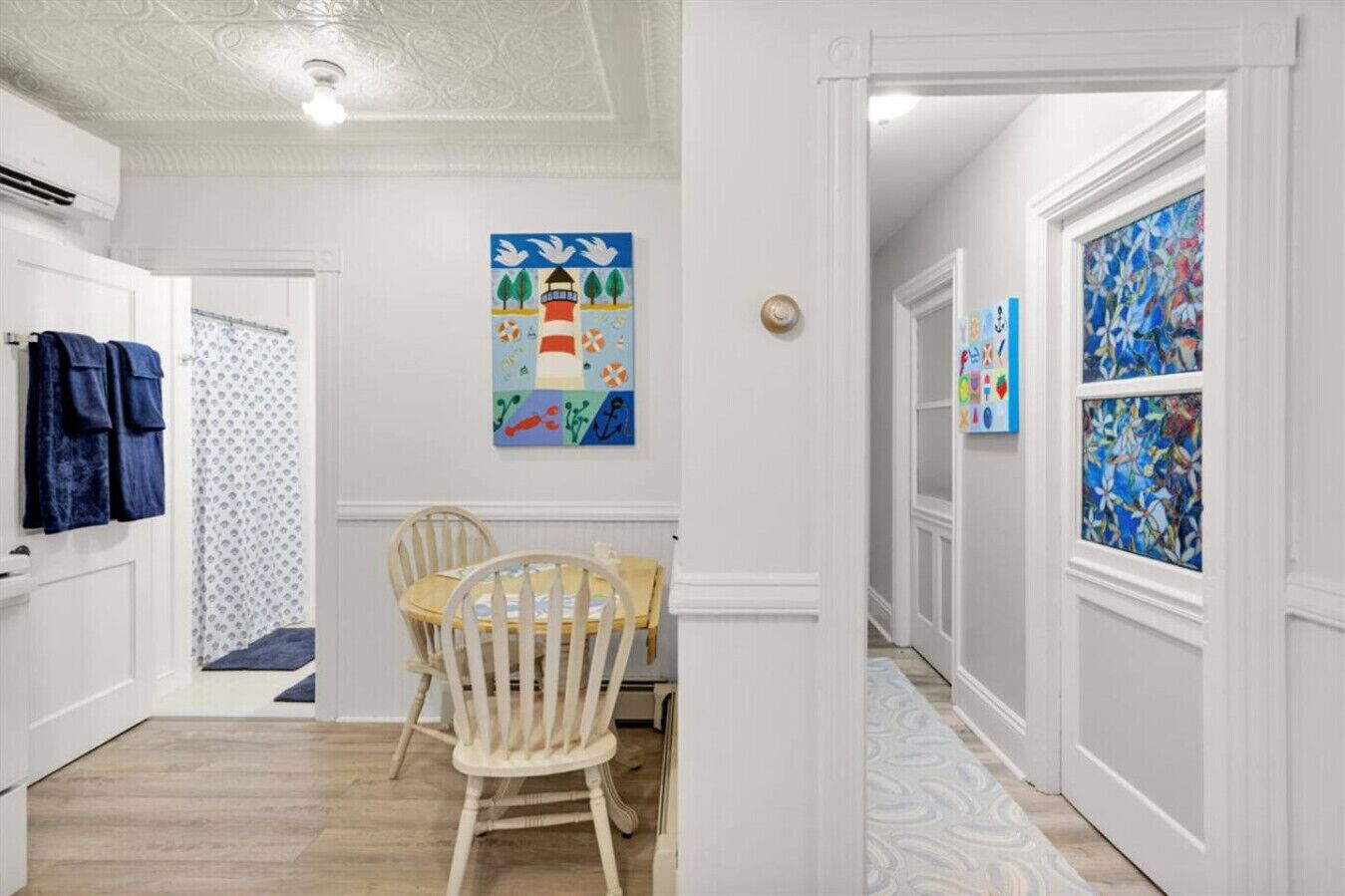 Un couloir comprenant un coin repas, avec une table et des chaises en bois, un tableau au mur et un tapis à motifs.