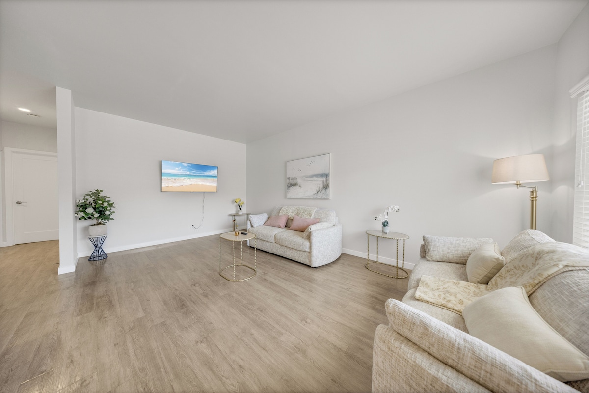 A spacious living room with a white sofa, a coffee table, and a lamp.