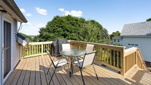 En träaltan med ett bord och stolar, en grill och utsikt över ett träd och ett hus.
