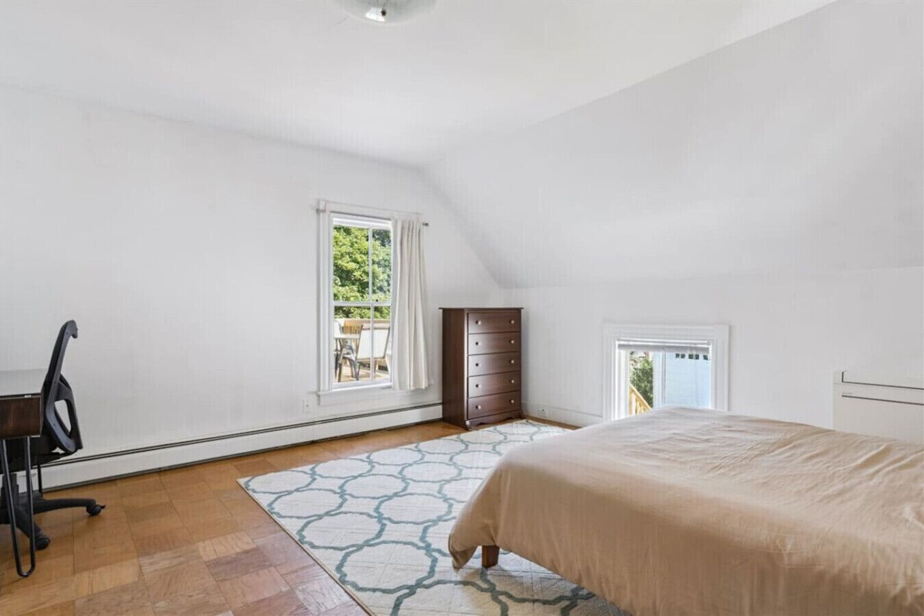 A bedroom with a bed, a dresser, a desk with a chair, a window, and a door.