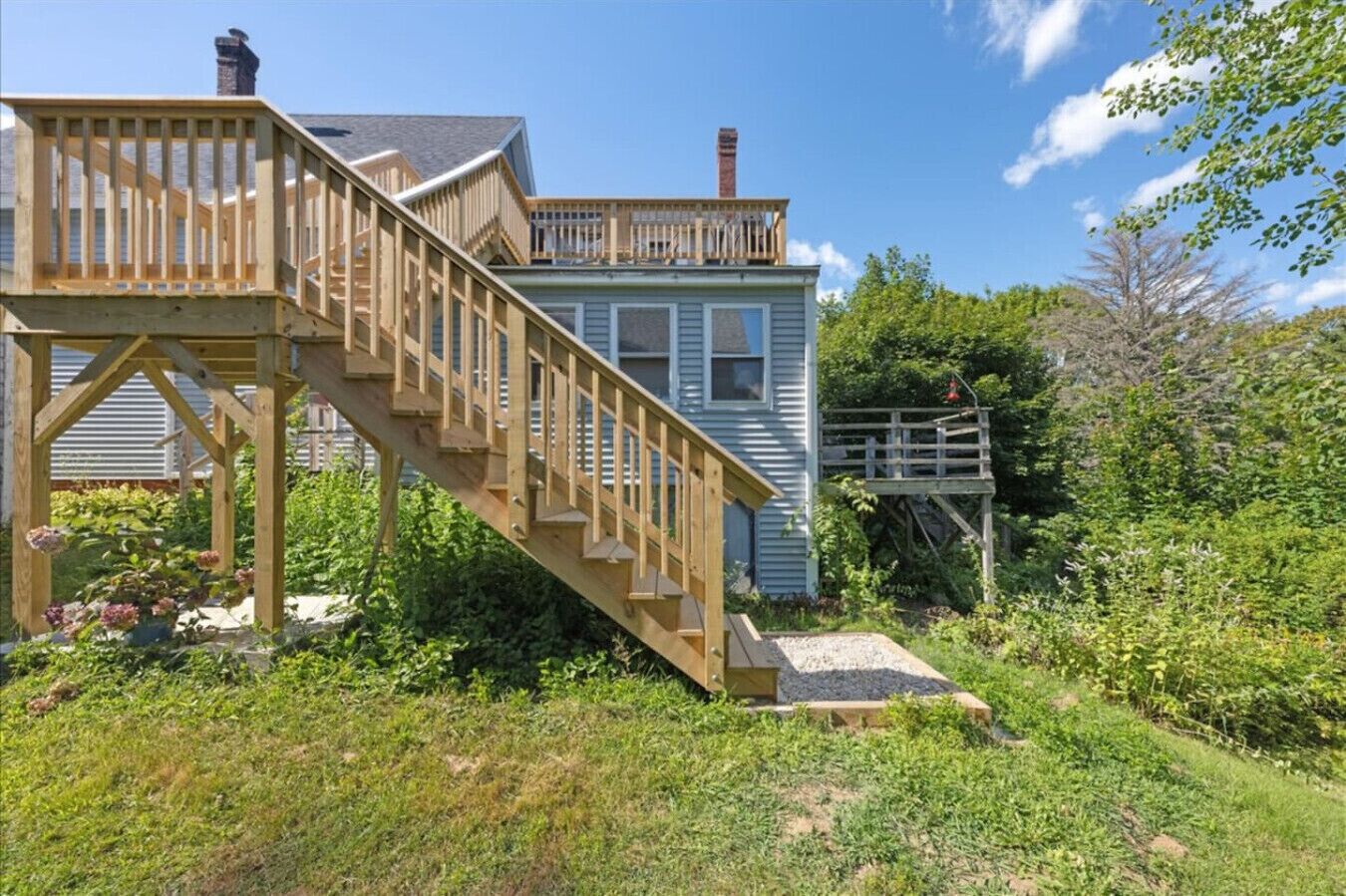 Une maison avec un escalier en bois menant à une terrasse, le tout entouré de verdure.