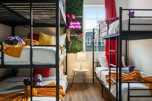 Ein Schlafsal mit Stockbetten, einem kleinen Tisch mit Lampe und einem Neon-Leuchtschild.