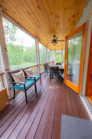 Eine überdachte Veranda mit Holzboden, einem Deckenventilator und einer Glastür, die nach draußen führt.