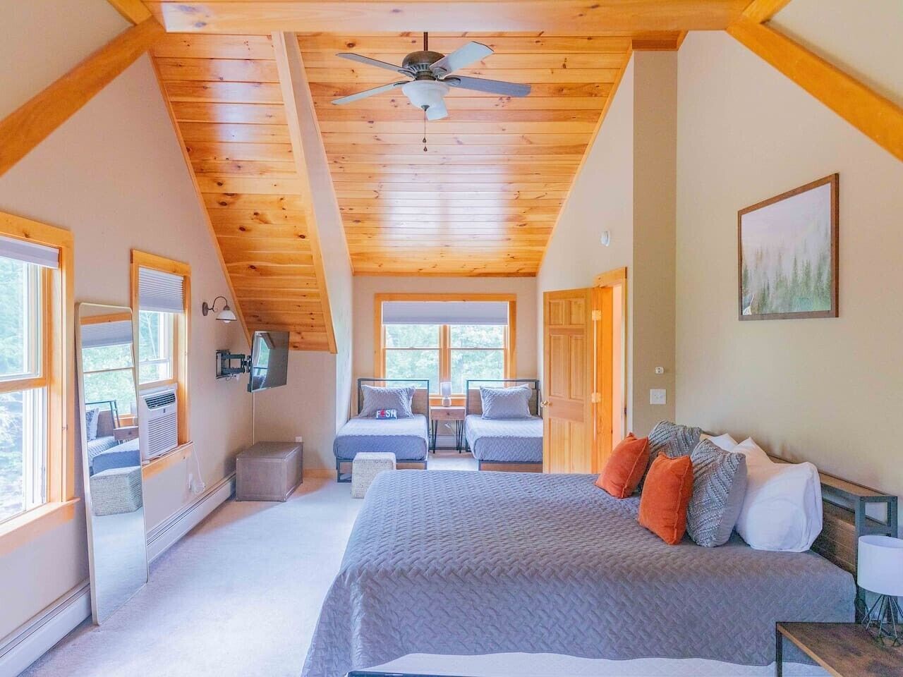 A bedroom with a large bed, two smaller beds, a ceiling fan, and a view of the outdoors.