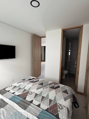 Ein Schlafzimmer mit einem Bett, einem an der Wand montierten Fernseher und einer offenen Tür zu einem Badezimmer.