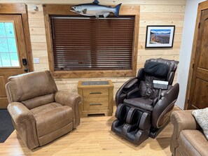 A room with a massage chair, a leather sofa, a wooden cabinet, and a large window with blinds.