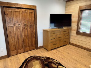 A room with a wooden wardrobe, a TV on a wooden cabinet, and a window with blinds.