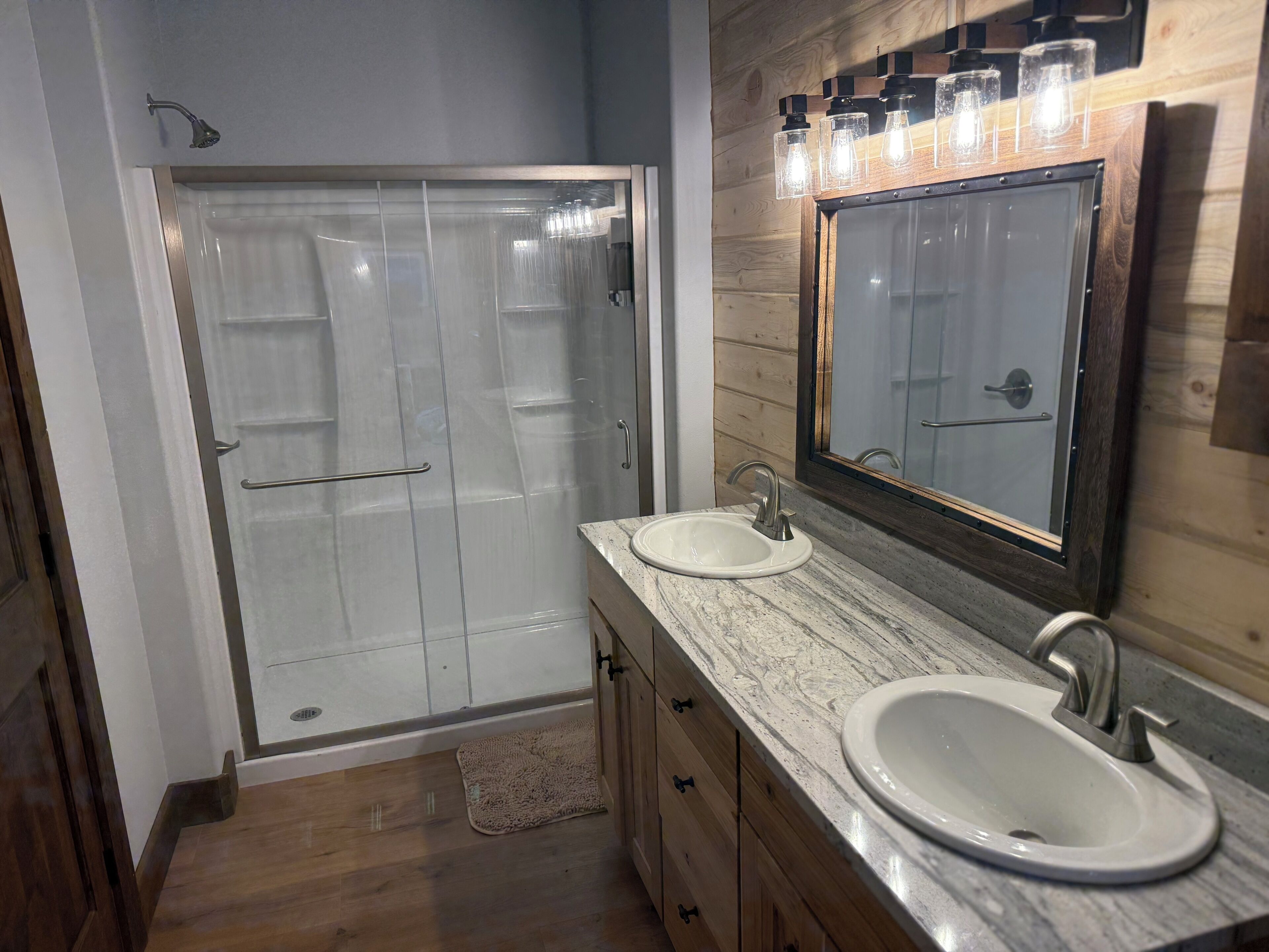 Een badkamer met een douchecabine van glas, een wastafel met een marmeren blad en een spiegel met verlichting erboven.