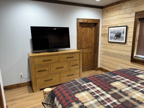 Un dormitorio con un aparador de madera, un televisor encima y una colcha a cuadros, además de un cuadro en la pared.