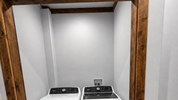 A laundry room with two white front-loading washers and dryers, wooden beams above, and a wooden floor. - SOLDOTNA SILVER TIP LODGE —  Authentic Alaska Log Lodge Near World-Class Fishing (Soldotna)