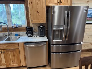 A stainless steel refrigerator with a water dispenser, a coffee maker, and a dishwasher in a kitchen with wooden cabinets and a window.