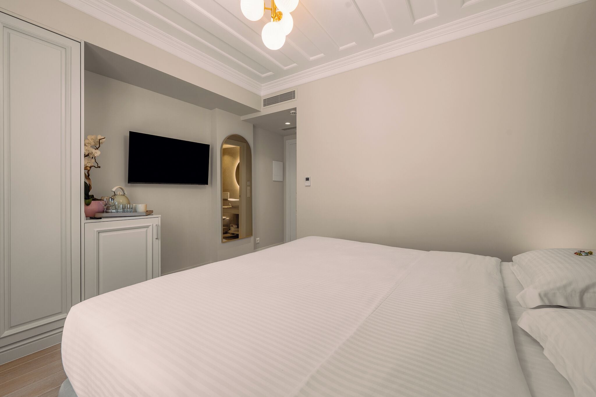 Ein Schlafzimmer mit einem großen Bett, einem an der Wand montierten Fernseher, einem Kleiderschrank und einem Schminktisch mit Spiegel.