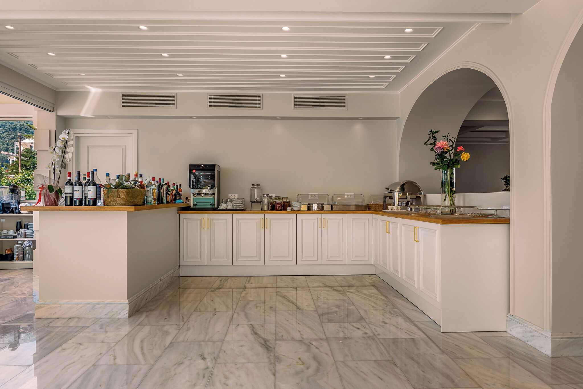 A modern kitchen with marble flooring, a central island with bar amenities, and a view through an arched doorway.