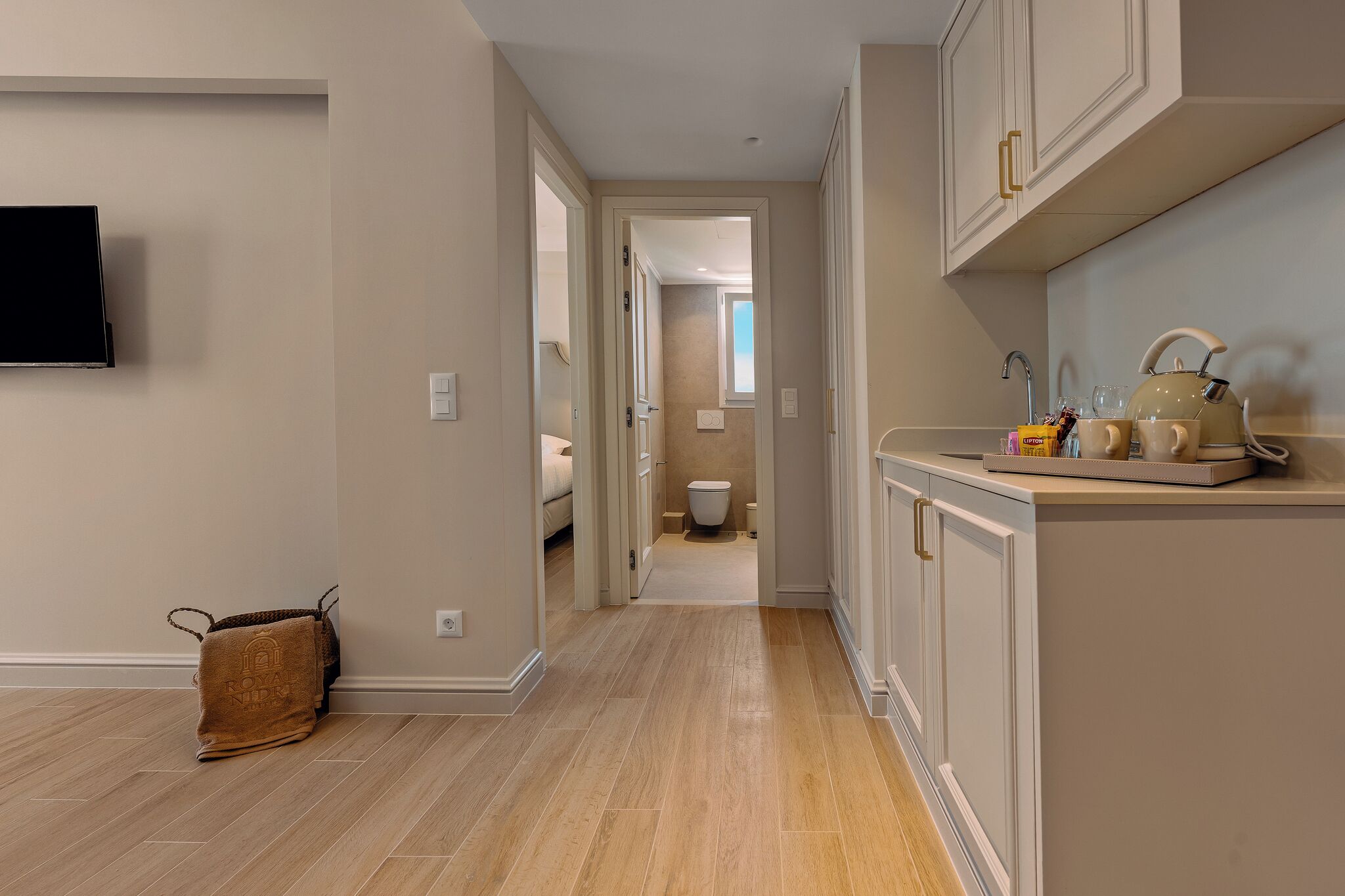 A hallway with a TV, a bag, a kitchen area with a kettle, and a toilet visible in the background.