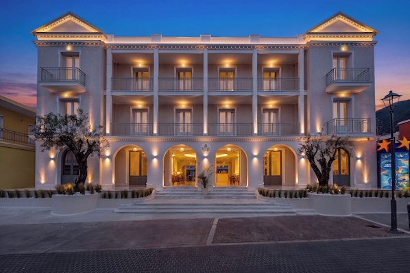 A multi-story hotel with balconies, arched entrances, and a well-lit facade.