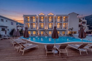 A hotel with a swimming pool, lounge chairs, and umbrellas.