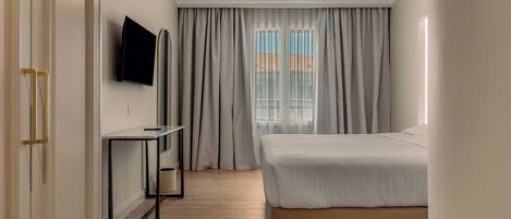 A bedroom with a bed, a TV, a desk, and a window with curtains.
