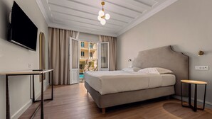 A modern hotel room with a bed, a TV, a desk, and a view of the outside. - Royal Nidri Suites (Nidri)
